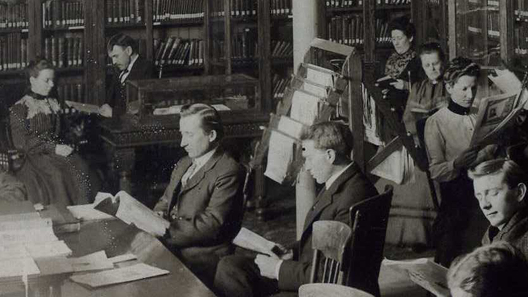 A black and white photo of people reading.